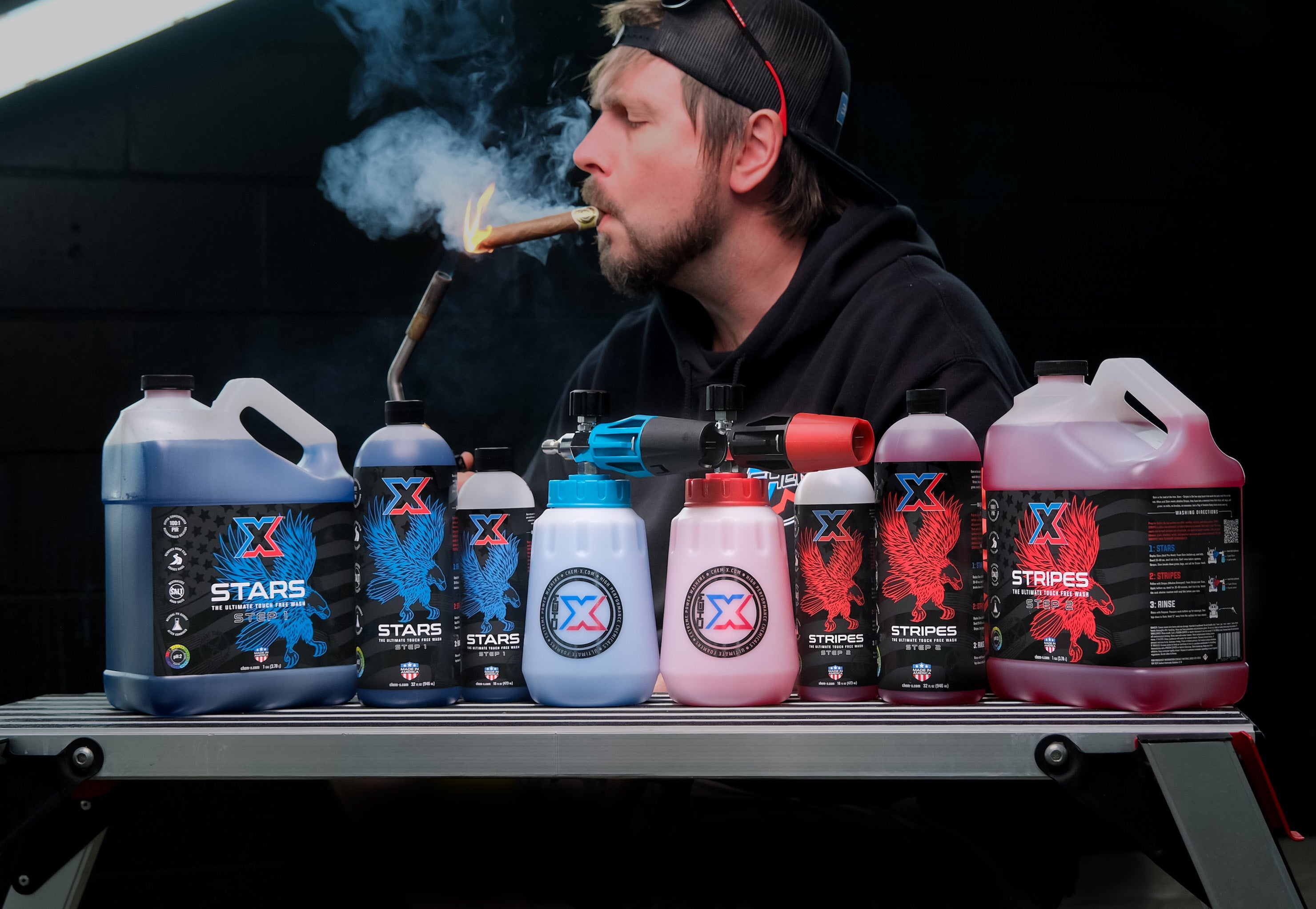 Line-up of Stars + Stripes bottles with foam cannons on a work bench. Bob smoking a cigar above.