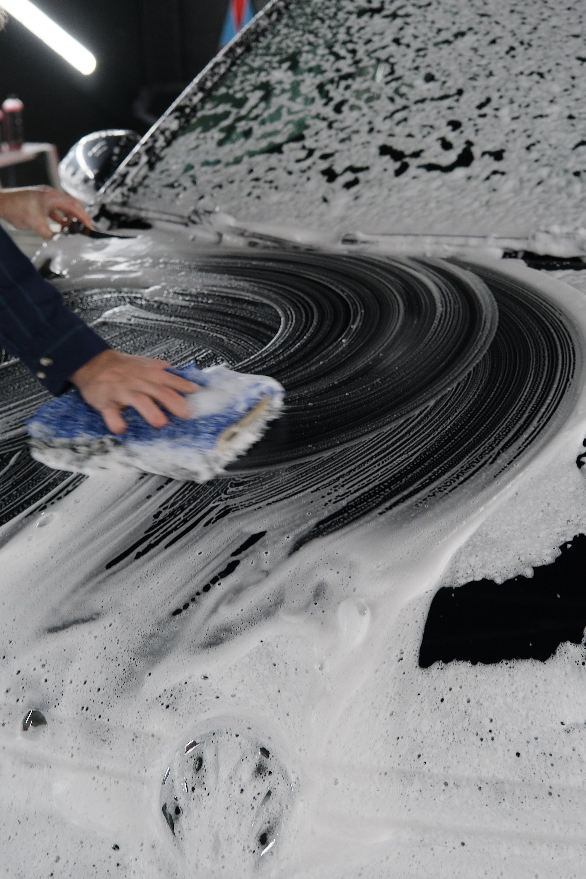 Person scrubbing down the hood of a car with foaming soap and a mitt.