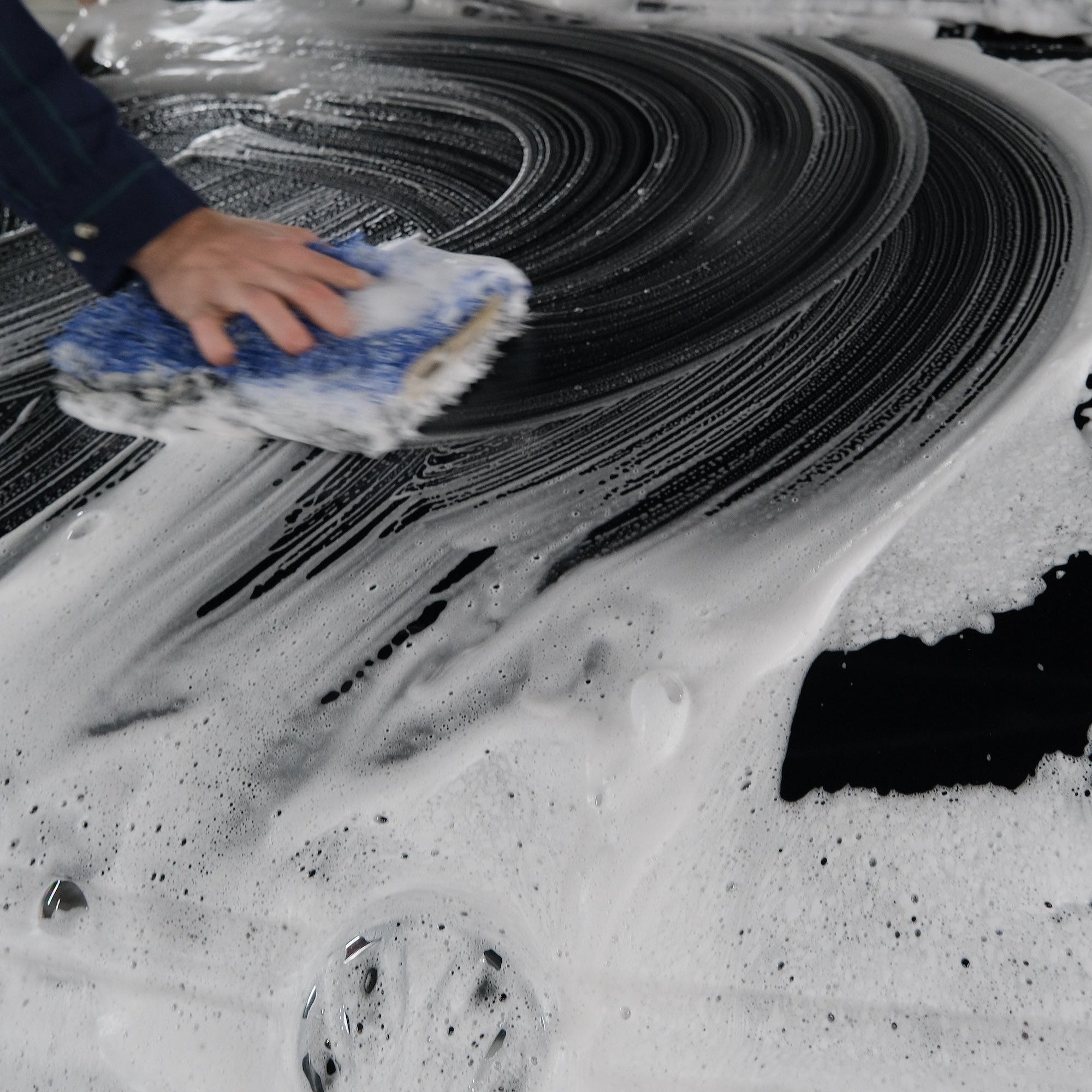 Person scrubbing down the hood of a car with foaming soap and a mitt.