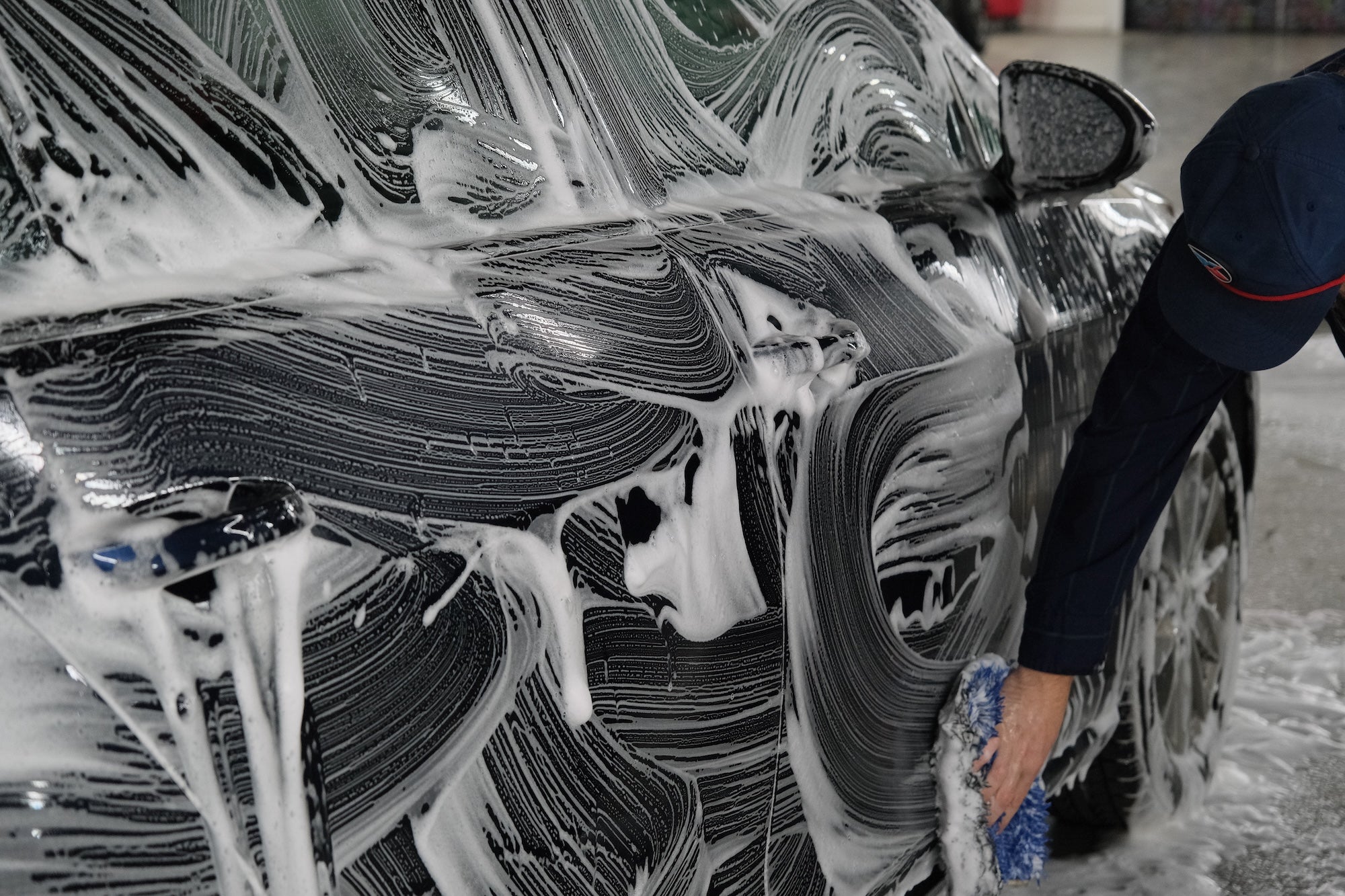 Person using a mitt to scrub a dark blue car down with soap.