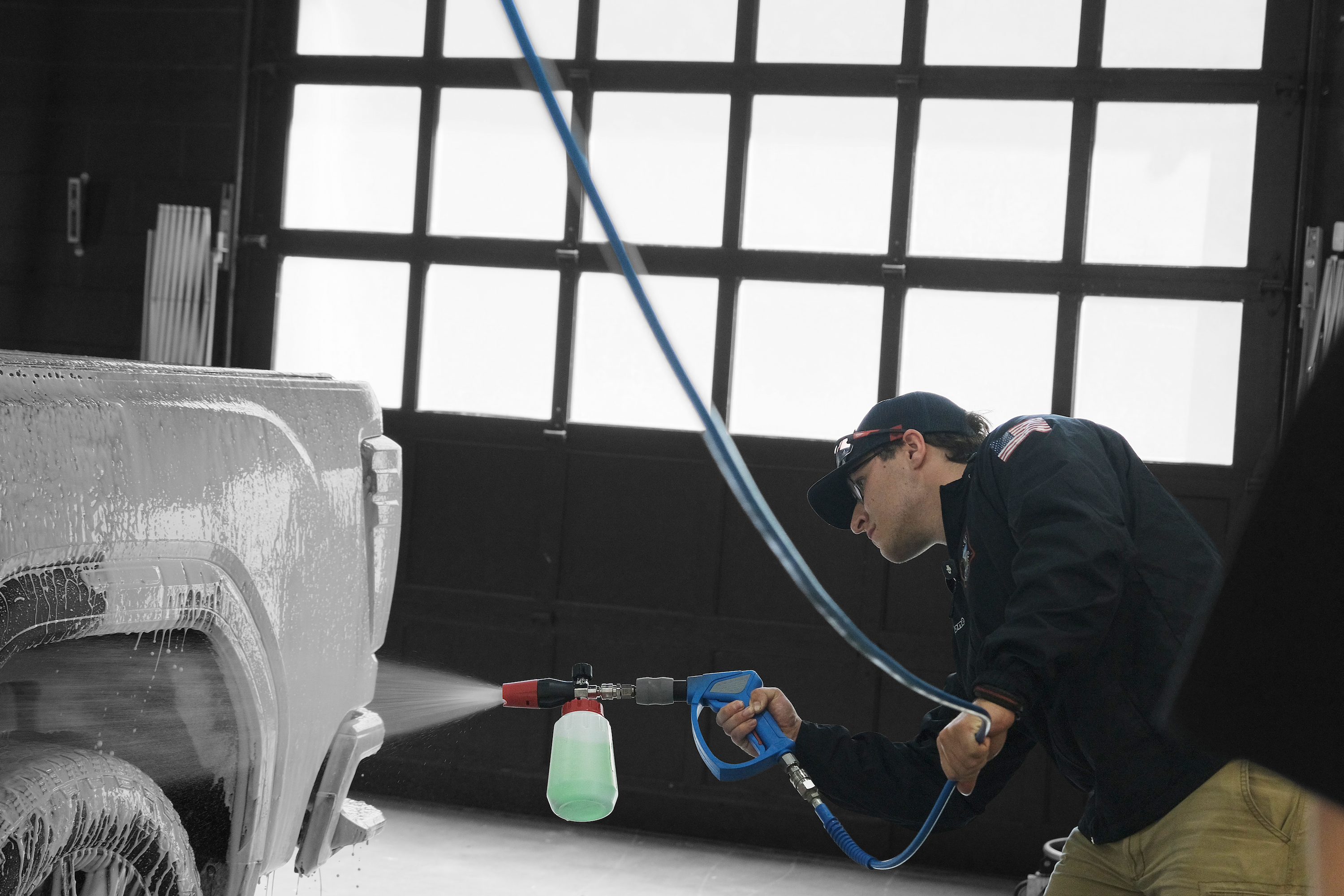 Person using a foam cannon attached to a pressure washer to apply foaming graphene sealant onto a truck in a wash bay setting.