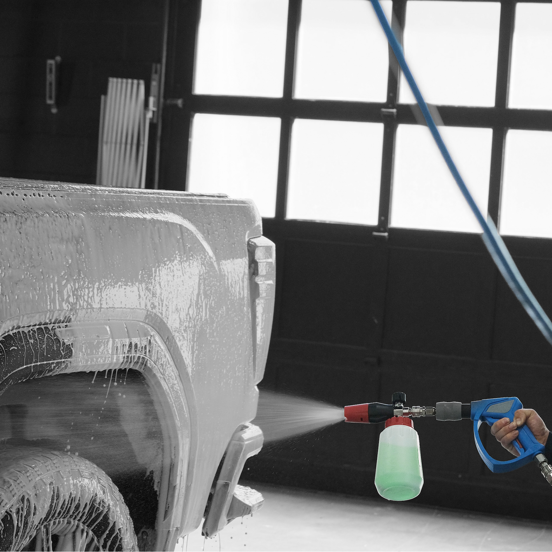 Person using a foam cannon attached to a pressure washer to apply foaming graphene sealant onto a truck in a wash bay setting.