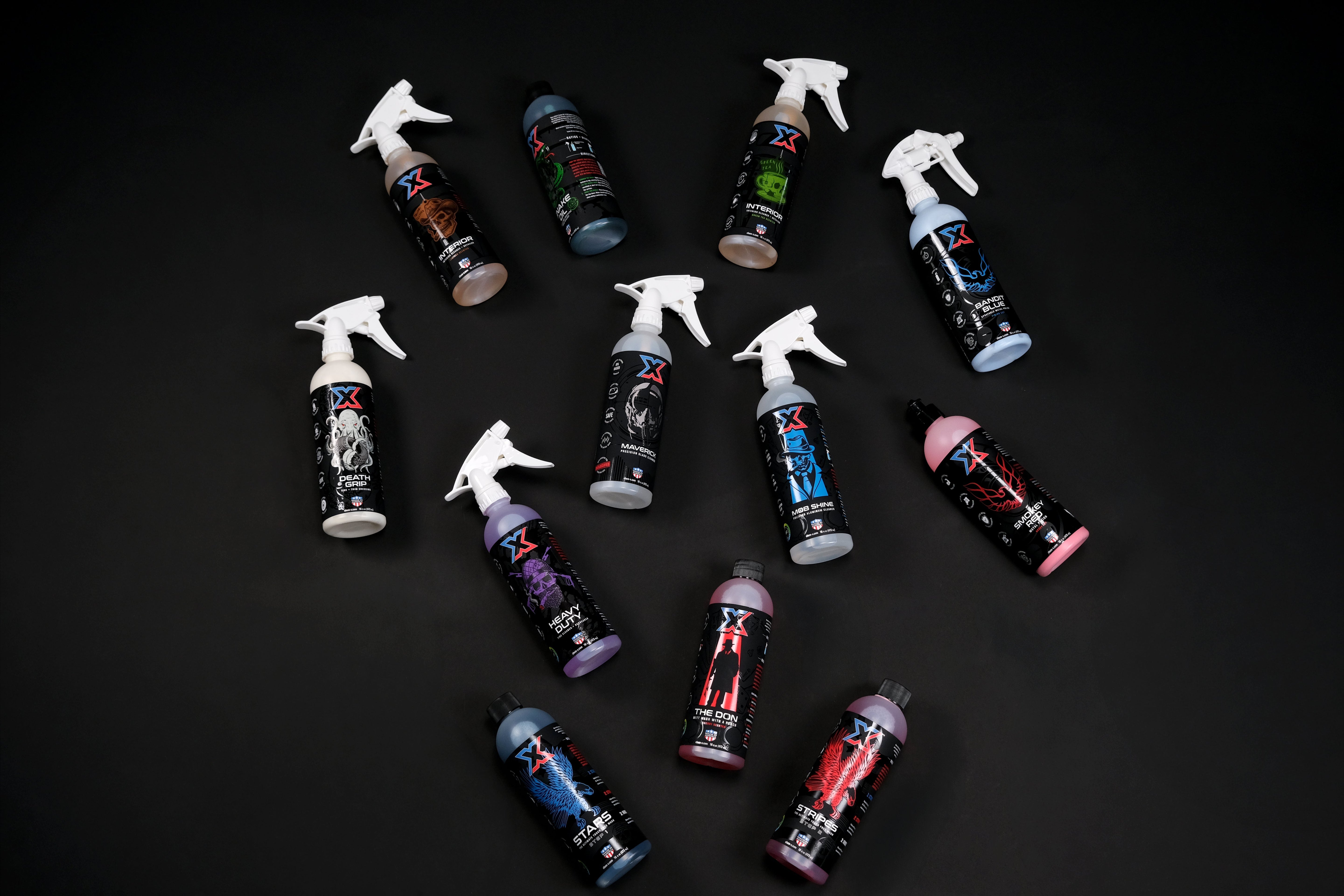 Twelve bottles filled with vehicle cleaning liquids with Chem-X branding on the labels lying on a black background in a scattered pattern.