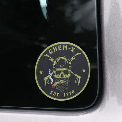 A circular black and green decal sticker featuring a skull with a hard hat, a beard, crossed lances, a burning cigar and the text 'CHEM-X EST. 1776', shown applied to a dark tinted truck window.