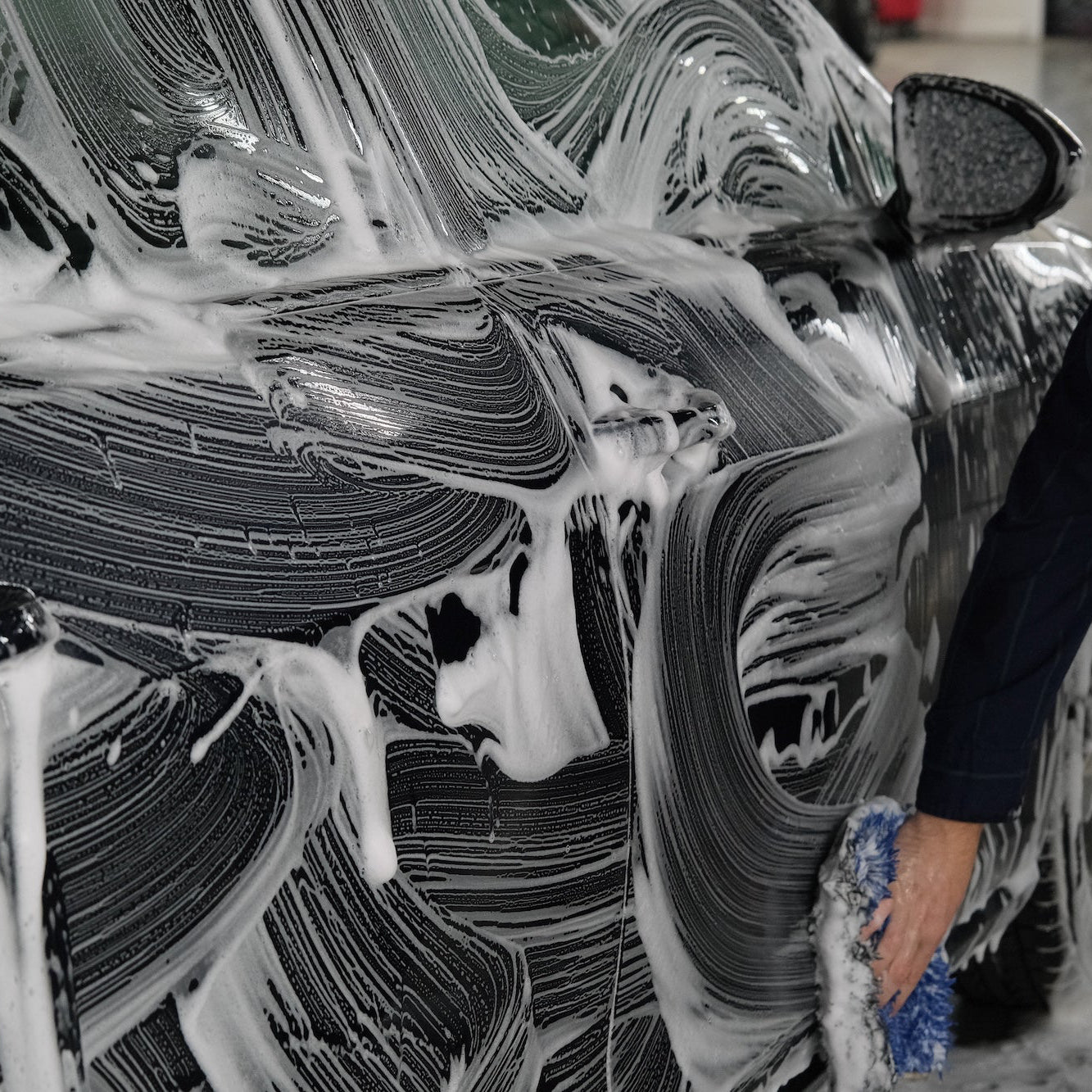 Person using a mitt to scrub a dark blue car down with soap.