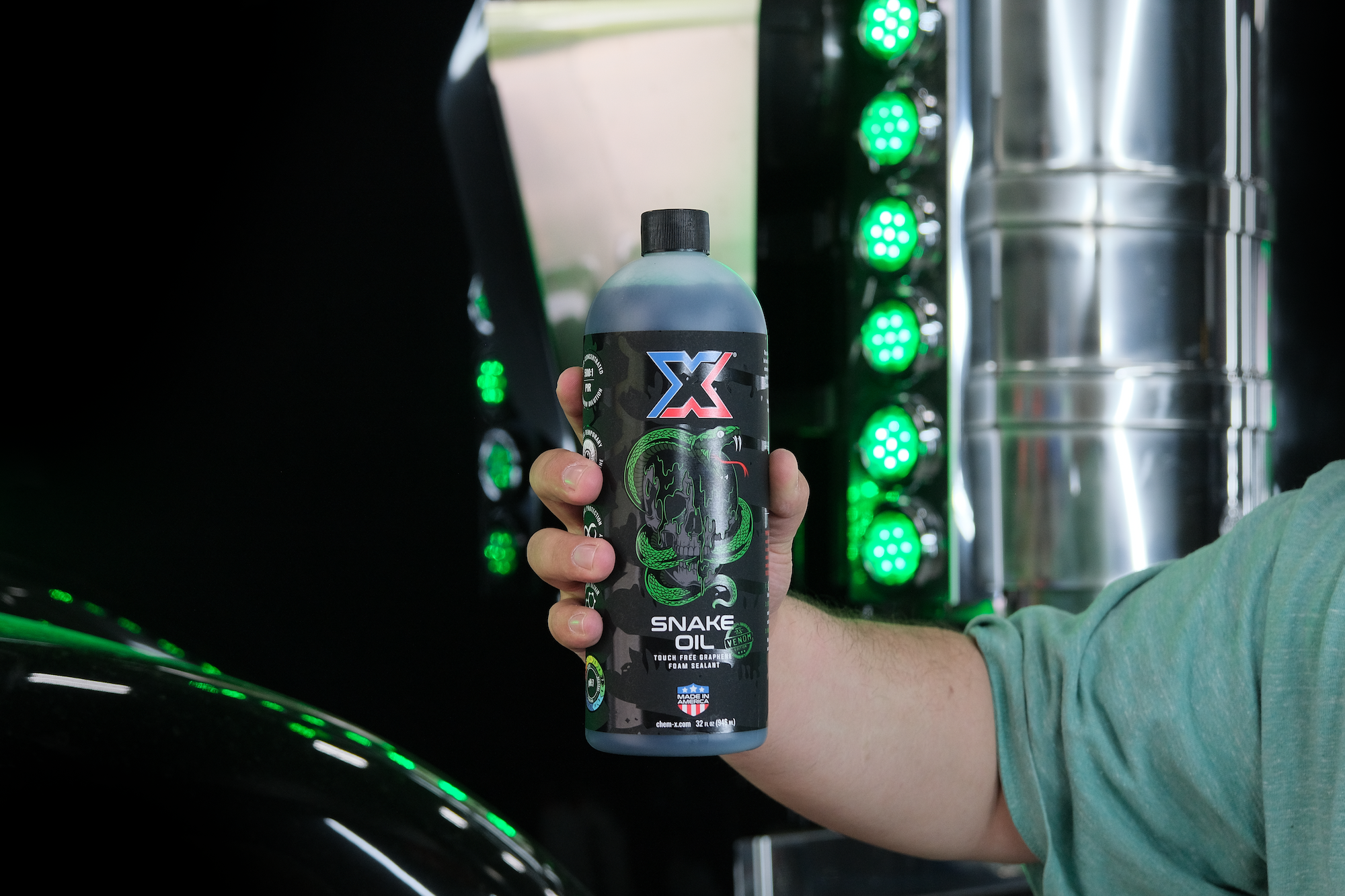 Hand holding Snake Oil Venom 32oz bottle with black and green truck in the background