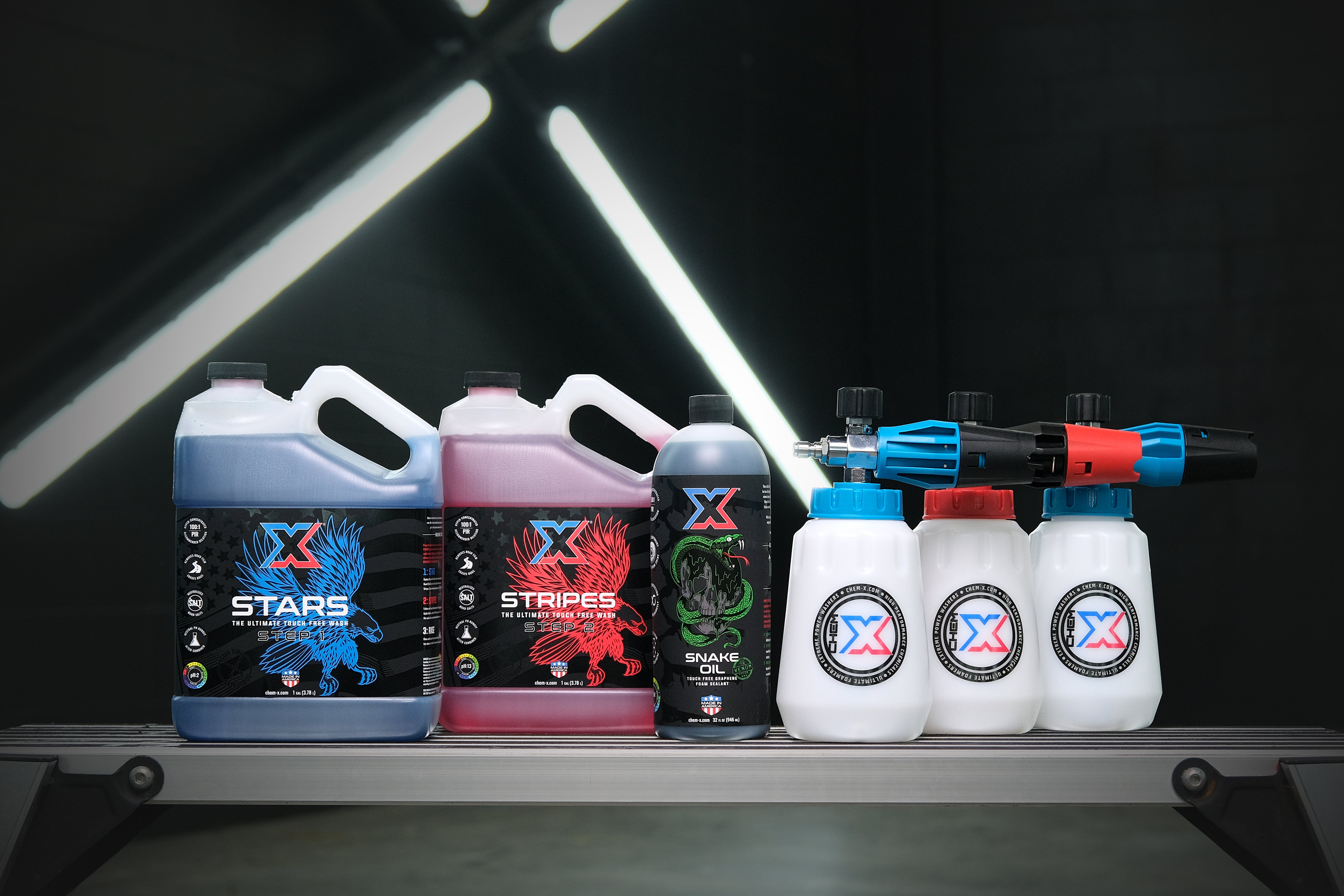 One gallon of blue liquid called 'Stars,' one gallon of red liquid called 'Stripes,' and one 32 oz bottle of green liquid called 'Snake Oil' on a workbench in a wash bay setting.