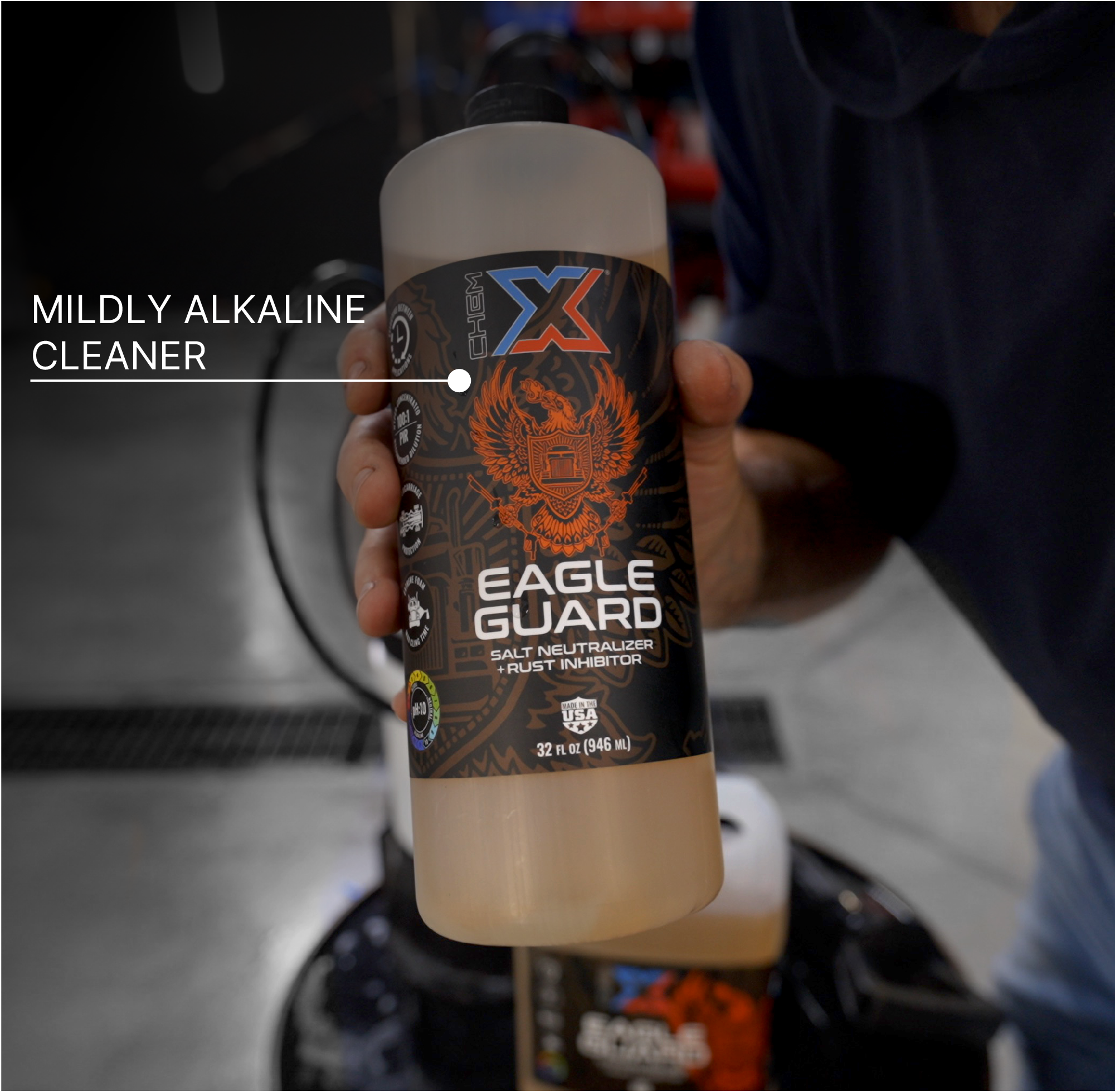 A hand holds a bottle of Chem-X Eagle Guard salt neutralizer and rust inhibitor with the text saying 'MILDLY ALKALINE CLEANER' overlaid across the top left of the image. The bottle has a black label with an orange eagle graphic and white text, and the liquid inside is a pale orange color.