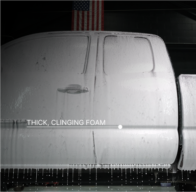 A close-up of a truck door covered in dripping foam, with the text 'THICK, CLINGING FOAM' overlaid across the lower middle. An American flag is faintly visible in the dark background above the truck.