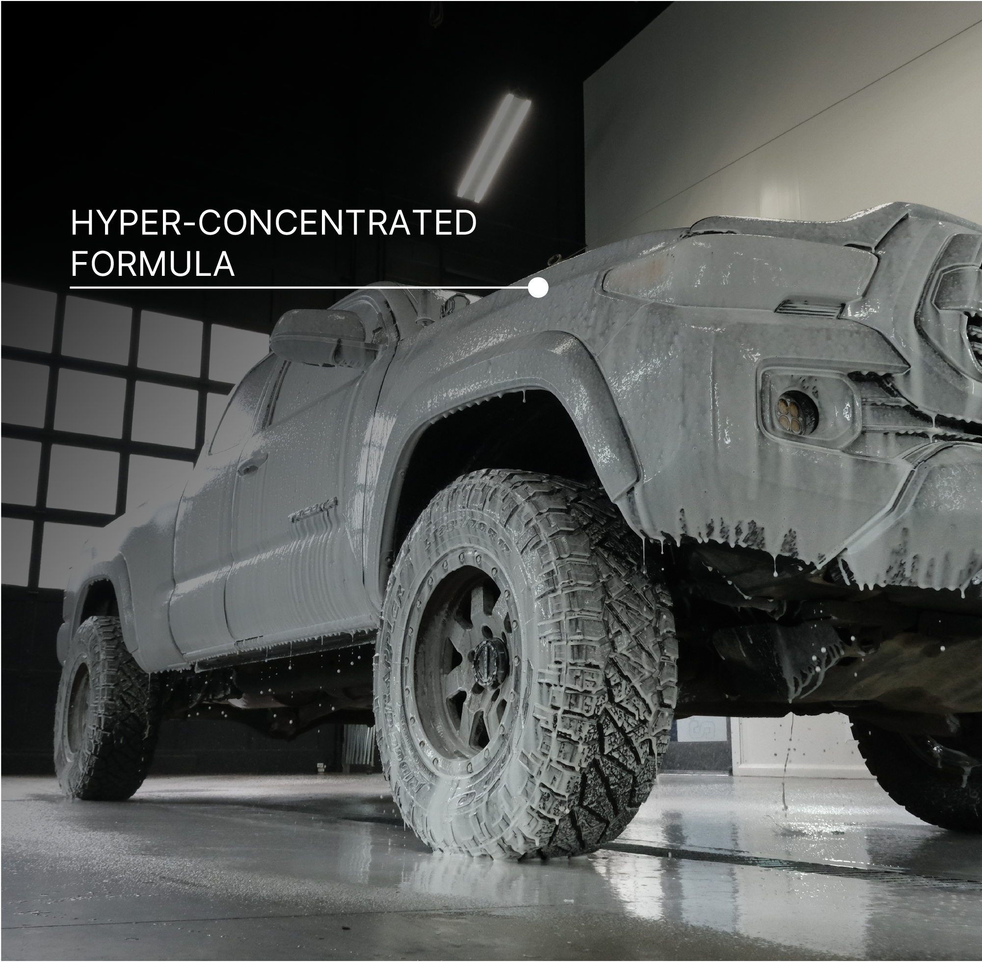 A gray off-road truck covered in white foam, photographed inside a dark wash-bay. Large text in the upper left reads 'HYPER-CONCENTRATED FORMULA.'