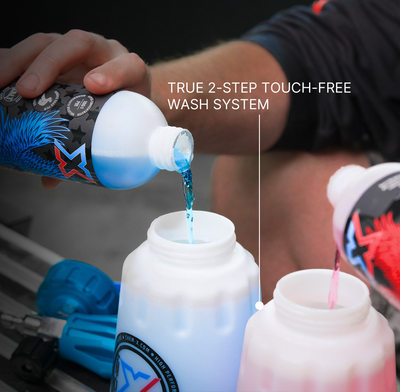 A close-up of a person pouring blue liquid from a Chem-X branded bottle into a white foam cannon, with another Chem-X bottle pouring red liquid into a foam cannon. White text reads 'TRUE 2-STEP TOUCH-FREE WASH SYSTEM.'